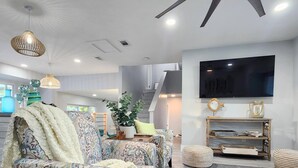 A modern living room with patterned sofas, a flat-screen TV, and a ceiling fan. - Hello Sunshine! 4 Bedroom w/Pool and Outdoor Bar (Tampa)