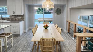 A modern kitchen with white cabinets, a wooden dining table with wicker chairs, and a large window overlooking a pool. - Hello Sunshine! 4 Bedroom w/Pool and Outdoor Bar (Tampa)