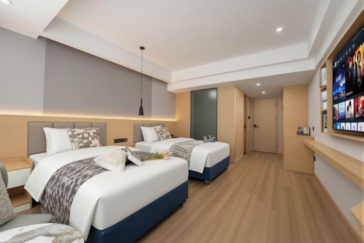 A modern hotel room with two beds, a TV, and a wooden floor.