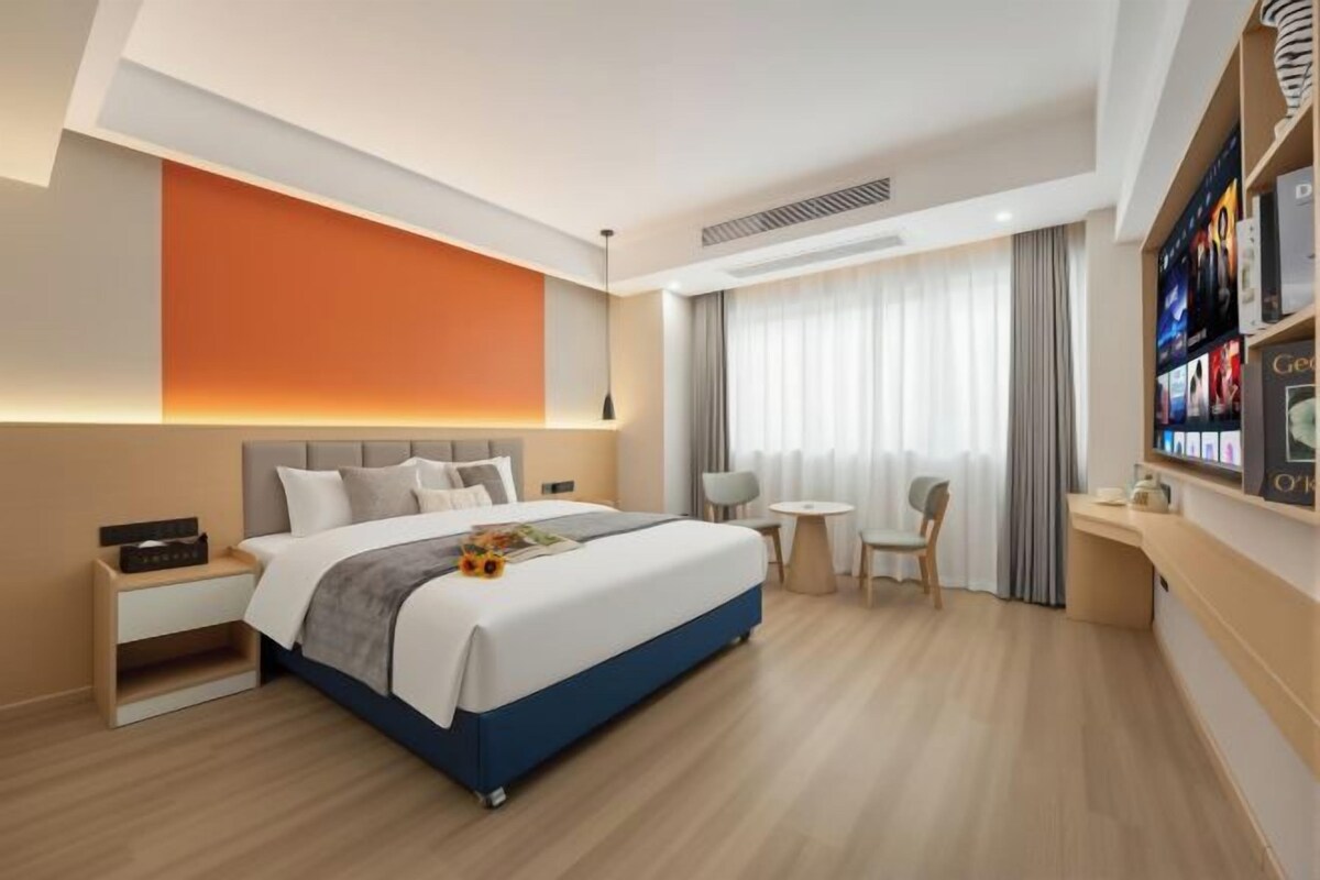A modern hotel room with a large bed, bedside tables, a small desk, and a seating area.