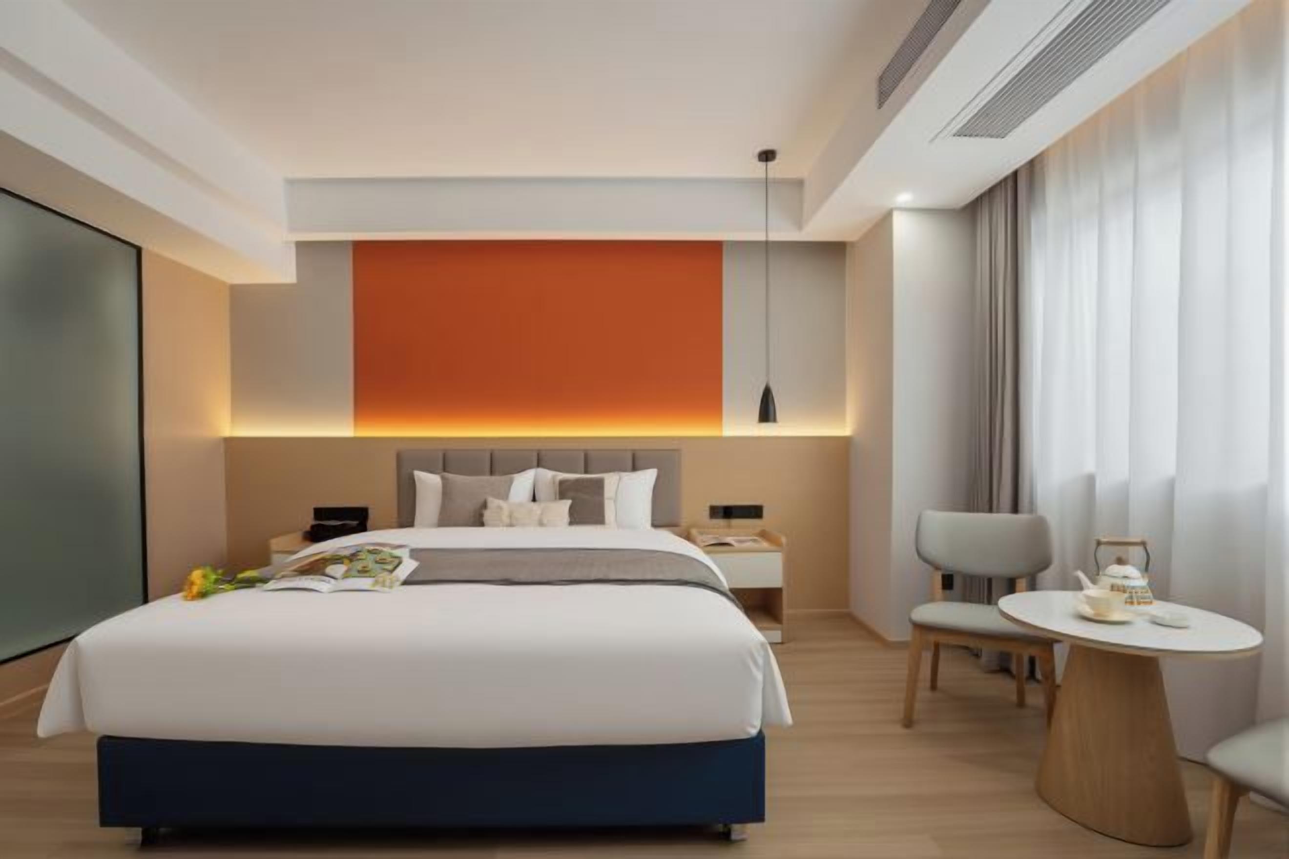 A modern hotel room with a large bed, bedside tables, a round table, and a view of the city.