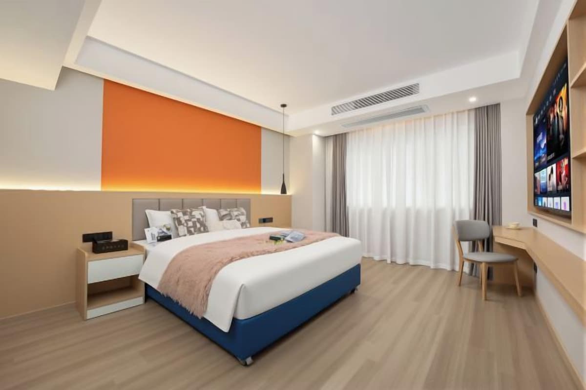 A hotel room with a bed, bedside table, chair, and a large window with curtains.