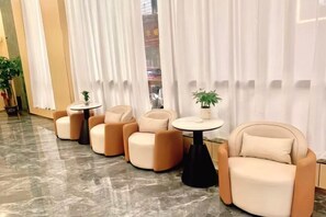 A seating area with cushioned chairs and small tables, a marble floor, and white curtains. - Ming Chao Holiday Hotel (Foshan)