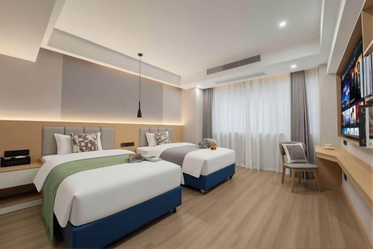 A modern hotel room with two beds, a desk, and a television.