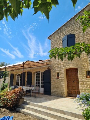 A stone building with a tiled roof, a wooden door, and a covered patio area with outdoor furniture.