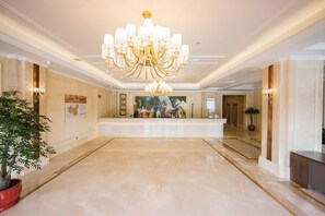 A spacious lobby with a grand chandelier, a reception desk, and a large painting on the wall.