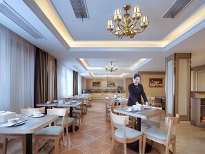 Un comedor de hotel con varias mesas y sillas, una araña y una persona de pie cerca de la entrada.