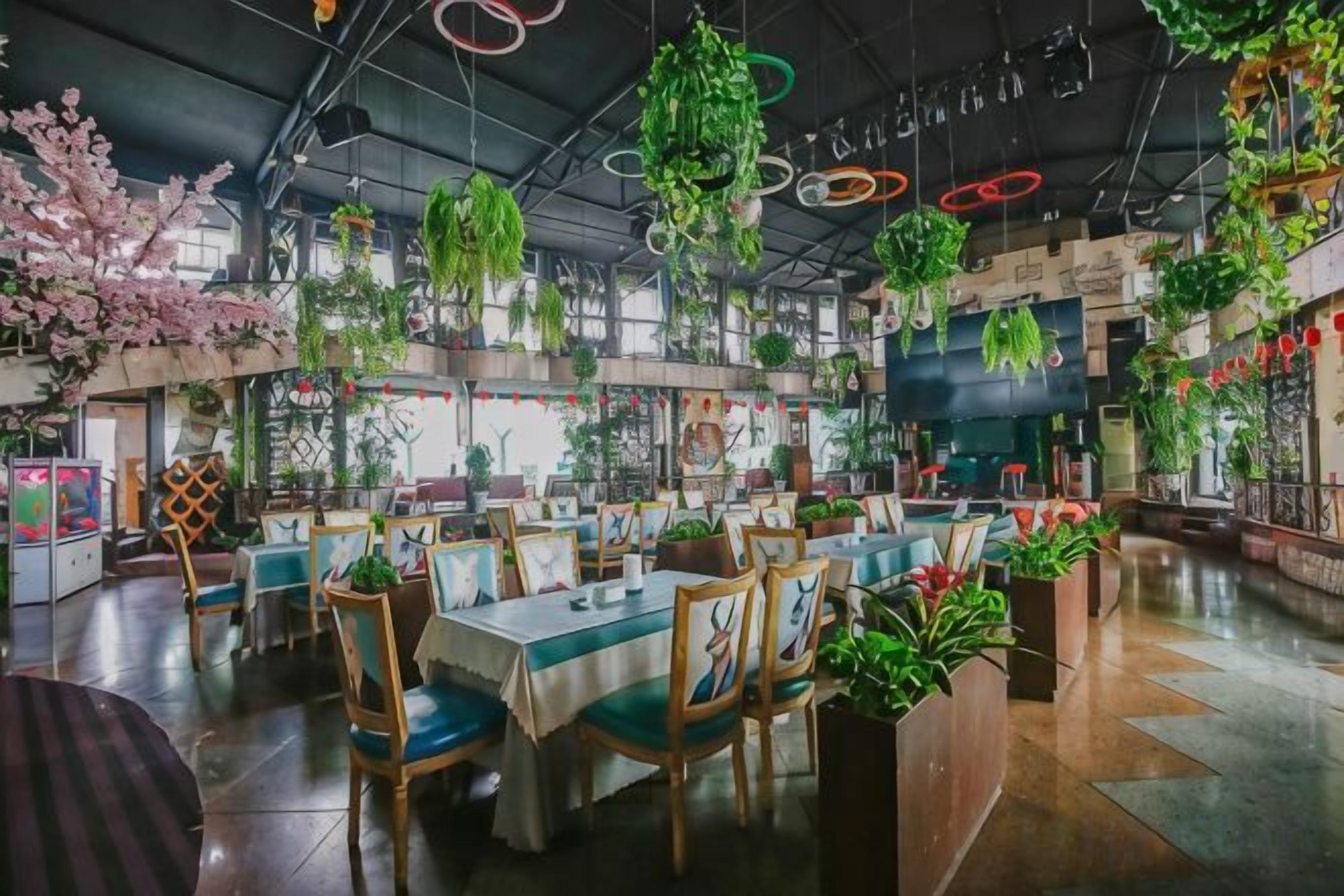 A restaurant with multiple tables and chairs, surrounded by hanging plants and greenery.