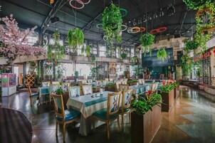 Un restaurante con varias mesas y sillas, rodeado de plantas colgantes y follaje.