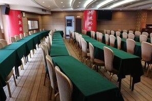 Un salón de conferencias con filas de mesas y sillas, un escenario y un estandarte rojo con texto blanco.
