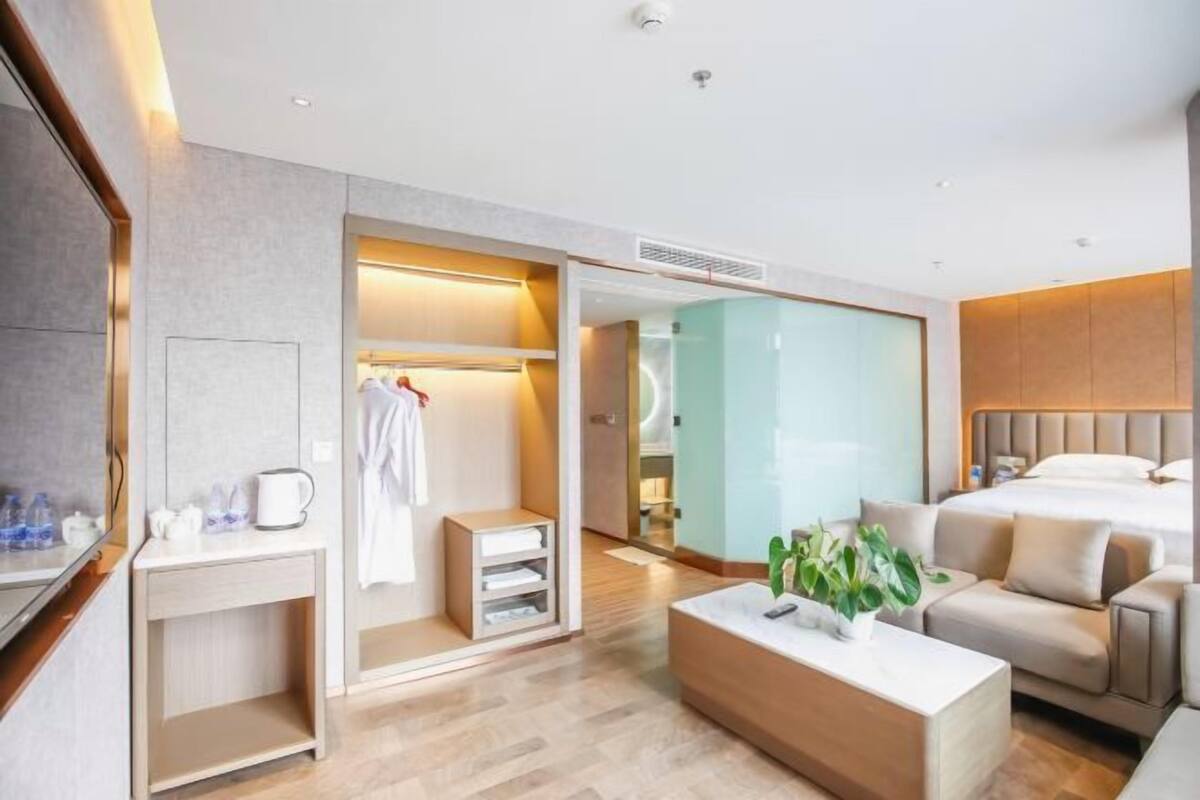 Ein modernes Hotelzimmer mit Bett, einer Sitzecke, einem Kleiderschrank und einem durchgegangene Tür erkennbaren Badezimmer.