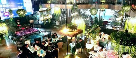 Un espacio interior con varias zonas de comedor, mesas y sillas, rodeado de plantas y follaje.
