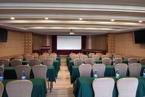 A conference room with rows of tables and chairs, a projector screen, and a screen at the front. - Tiancheng Plaza Hotel (Neijiang)