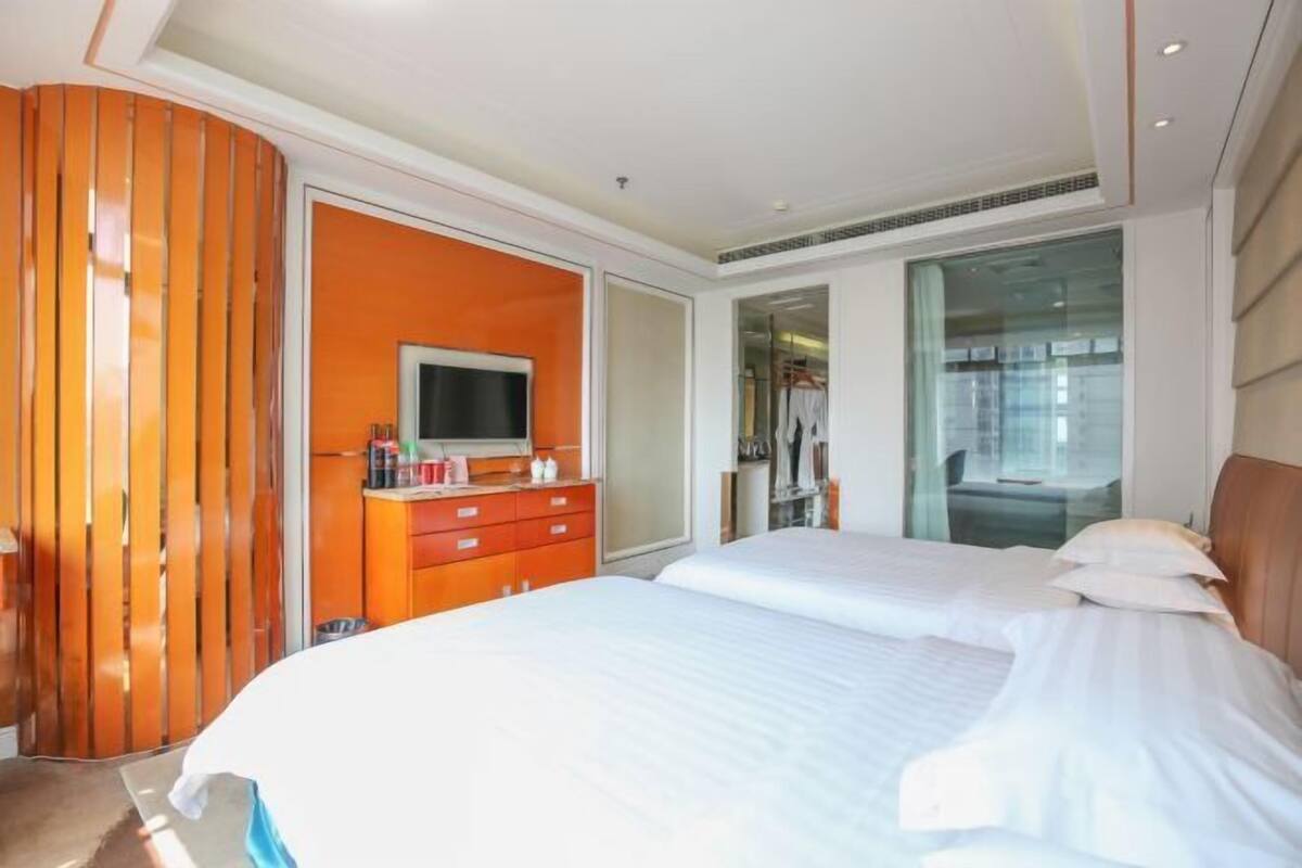 Ein Hotelzimmer mit zwei Betten, einem Fernseher, einem Kleiderschrank und einer Glastür zum Badezimmer.