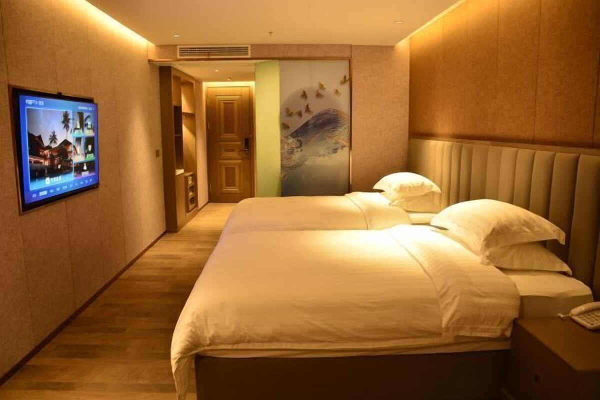 Een hotelkamer met twee bedden, een aan de muur bevestigde televisie en een deur naar een andere kamer.