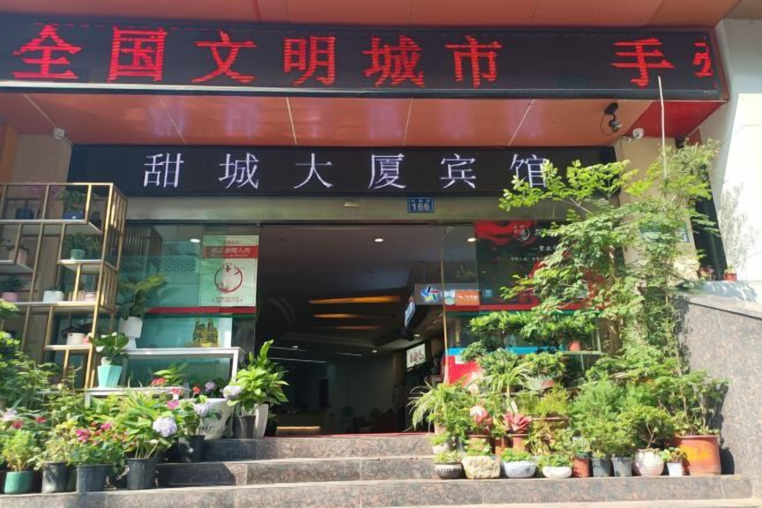 A building entrance with a sign in Chinese characters, potted plants, and a staircase leading up to the entrance.