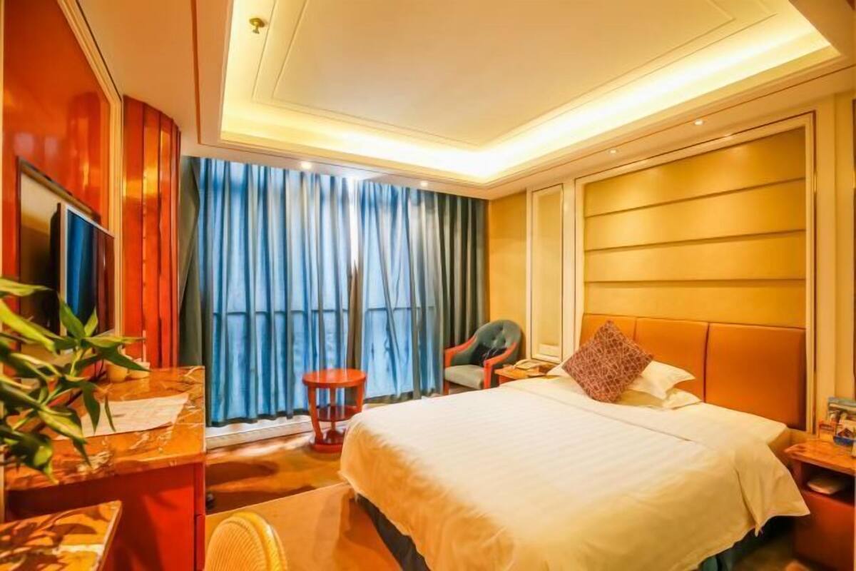 Ein Hotelzimmer mit Bett, Schreibtisch, Stuhl, Fernseher und einem Fenster mit Vorhängen.