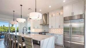 A modern kitchen with a large island, white cabinetry, stainless steel appliances, and pendant lighting.