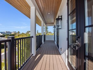 A covered porch with a wooden ceiling, black railings, and large windows.