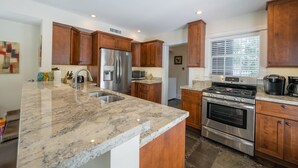 A modern kitchen with granite countertops, stainless steel appliances, wooden cabinets, and a window with blinds. - Papa's Casita in Downtown Key West (Key West)