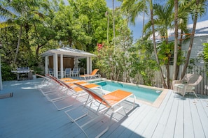 A pool area with lounge chairs and a covered seating area.