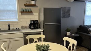 A modern kitchen with white cabinets, a stainless steel refrigerator, a coffee maker, and a dining table with chairs. -  The Bungalow on State (Eau Claire)