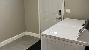 A laundry room with a washing machine, a door with a window, and a tiled floor. -  The Bungalow on State (Eau Claire)