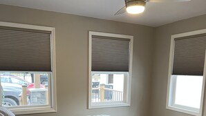 A bedroom with a bed, a ceiling fan, and three windows with blinds. -  The Bungalow on State (Eau Claire)