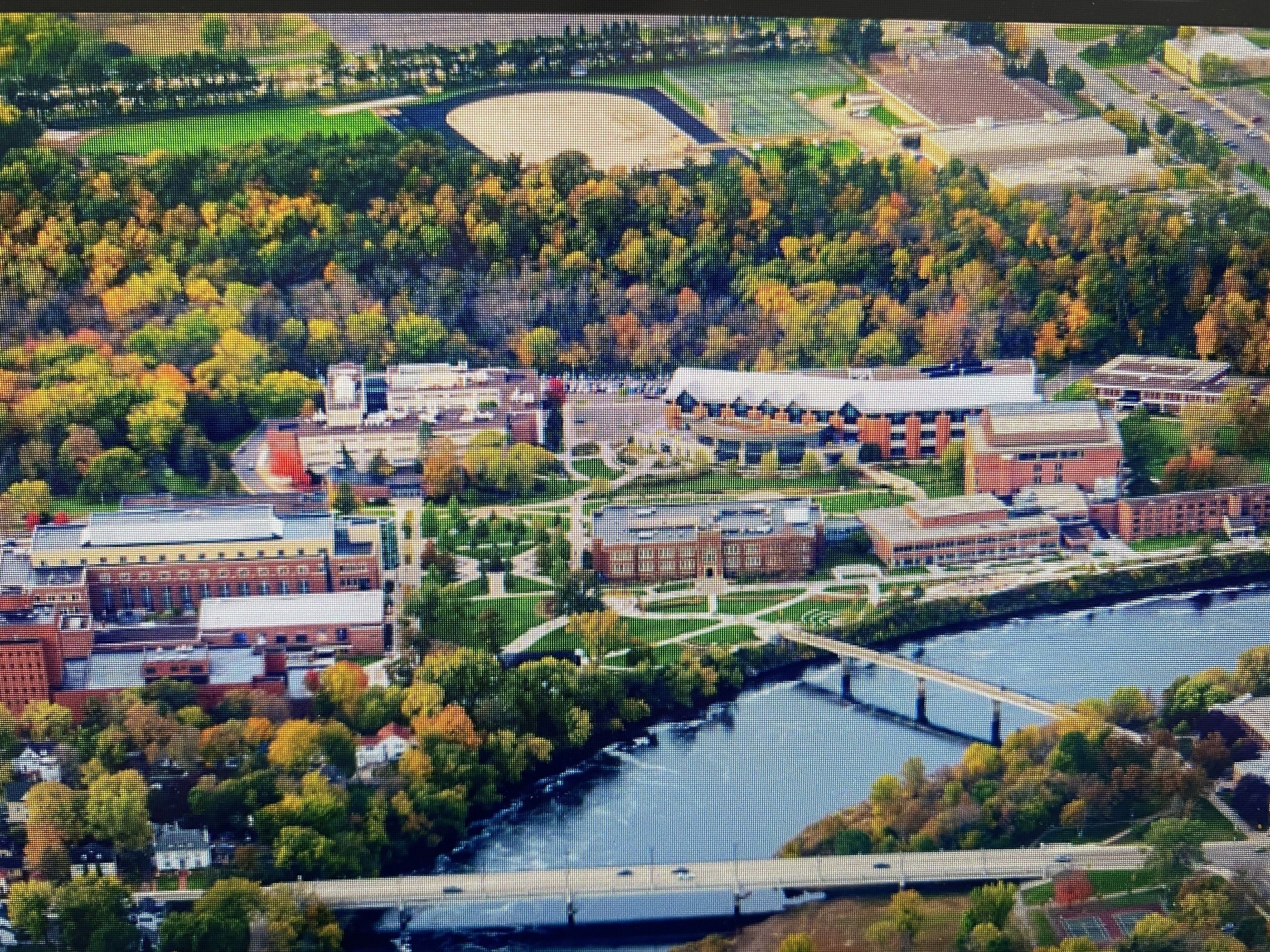 An aerial view of a campus with buildings, a river, and green spaces.