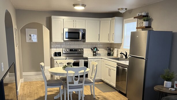 A modern kitchen with white cabinets, stainless steel appliances, and a dining area with a round table and chairs. -  The Bungalow on State (Eau Claire)