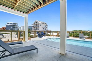 Uma área de piscina com espreguiçadeiras, um deck de madeira e vista para edifícios ao fundo.