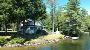 Une maison au bord du lac, dotée d’un porche abrité, d’un quai et d’un muret en pierre longeant le rivage.