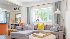 Un salon moderne avec un canapé d’angle gris, un pouf rond et une table basse en bois.