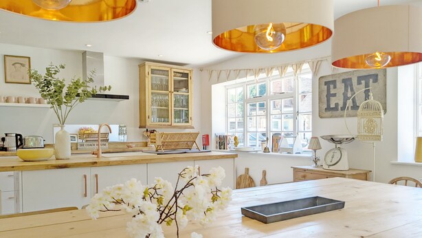 Une cuisine moderne avec un îlot central en bois, des meubles blancs et des luminaires suspendus.