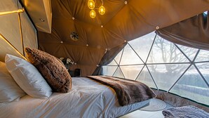 A cozy, well-lit tent-style bedroom with a bed, pillows, and a view through a large window. - Knole Luxury Dome (Hoath)