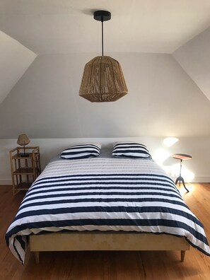Cozy retreat with a sloped ceiling, featuring a bed with striped bedding and a pendant light.
