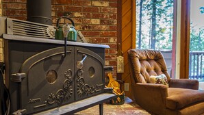 A brick fireplace with a bench, a leather armchair, and a window with a view of trees. - Evergreen Dorrington • Both Cabins • Game Room • Hot Tub • Pool Access (Dorrington)