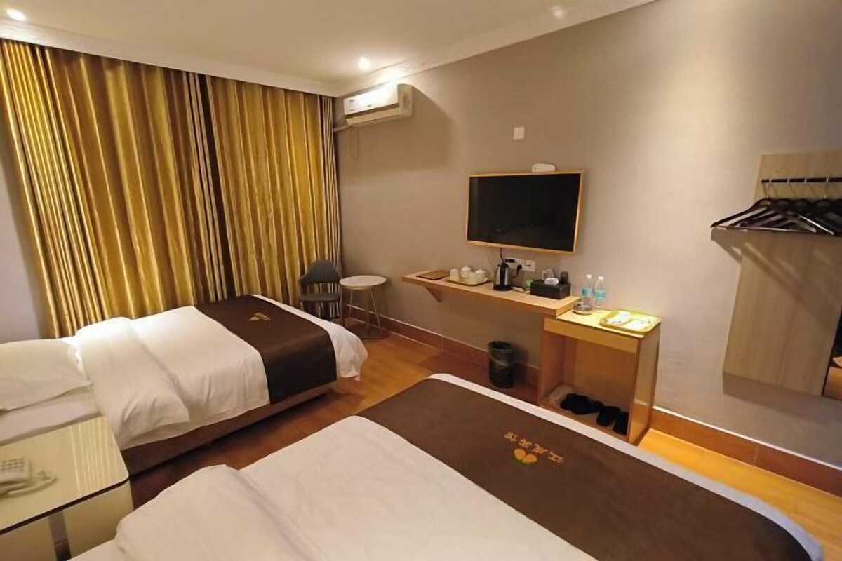 Habitación de hotel con dos camas, un escritorio con televisor de pantalla plana, una silla, una mesita de noche con artículos de aseo y un perchero.