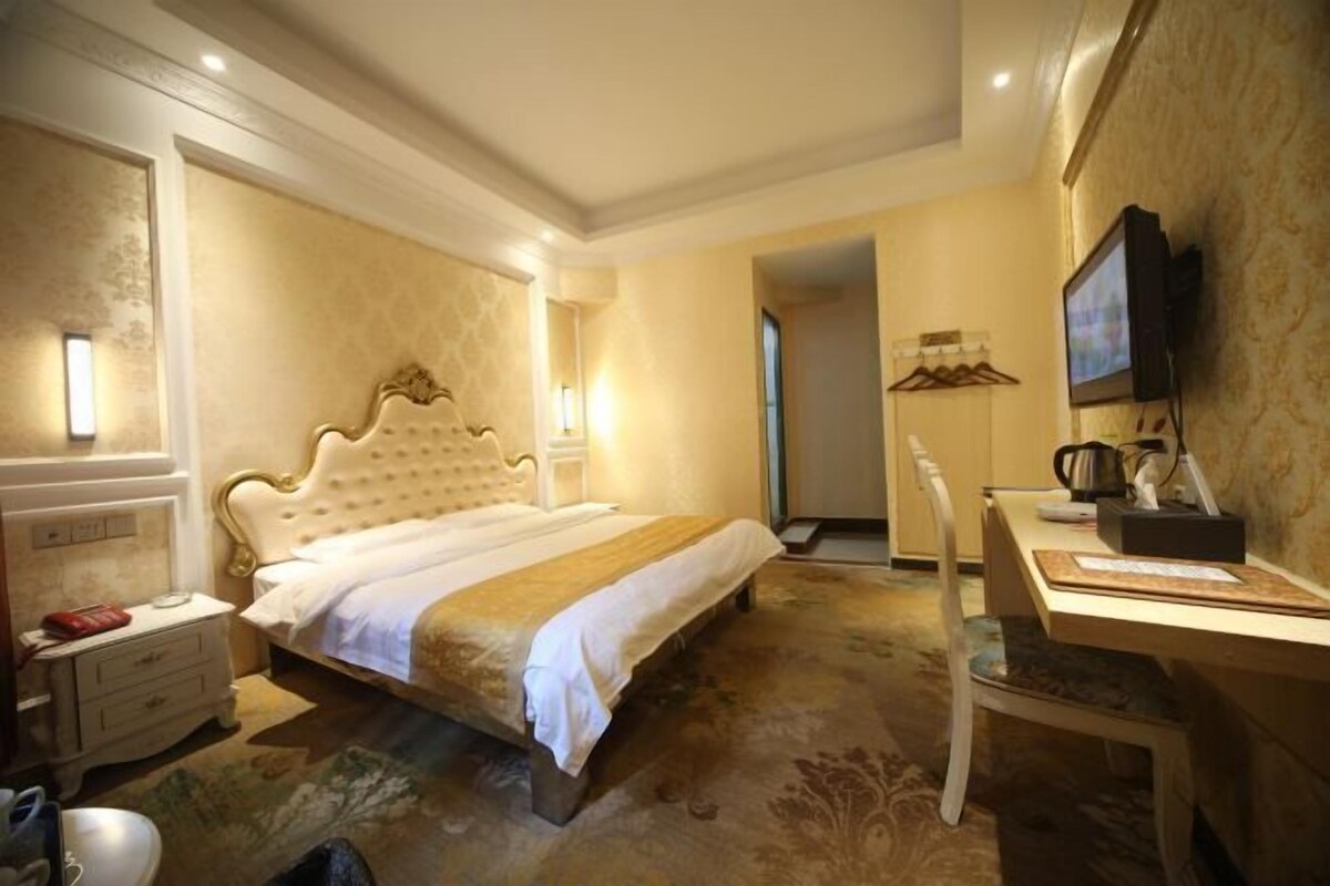 Una habitación de hotel con una cama grande, un escritorio, una silla, un televisor y un espejo.