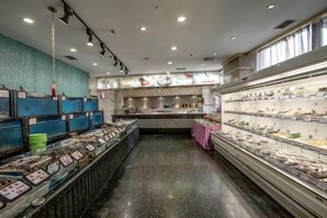 A seafood display area with various seafood items on shelves, a kitchen area with stainless steel appliances, and a counter with a pink tablecloth. - Rose Garden Hotel (Dalian)
