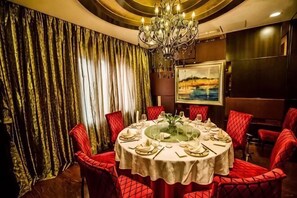 A dining area with a round table, red upholstered chairs, a chandelier, and a painting on the wall. - Rose Garden Hotel (Dalian)