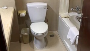 A small bathroom with a toilet, a trash can, and a bathtub. - Rose Garden Hotel (Dalian)