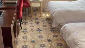 A hotel room with two beds, a small round table, a red chair, and a patterned floor. - Rose Garden Hotel (Dalian)