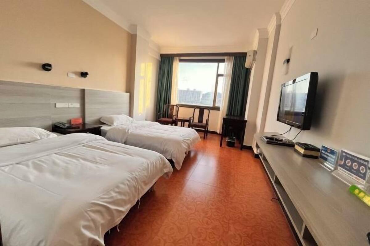 A hotel room with two beds, a TV, a desk, and a window with curtains.