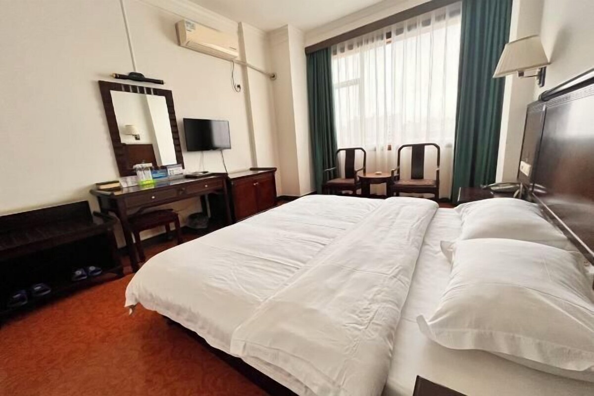 Habitación de hotel con una cama grande, un escritorio con silla, un televisor y una ventana con cortinas.