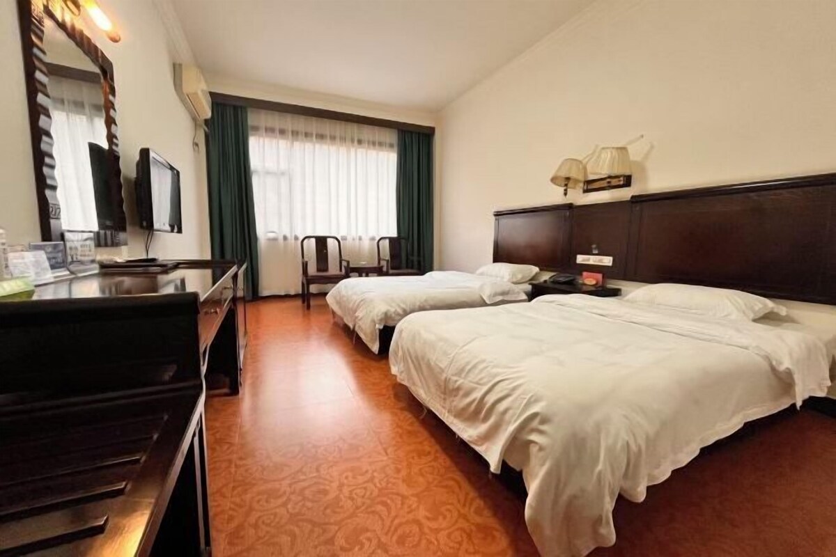 Habitación de hotel con dos camas, un escritorio, televisión, espejo y ventana con cortinas.
