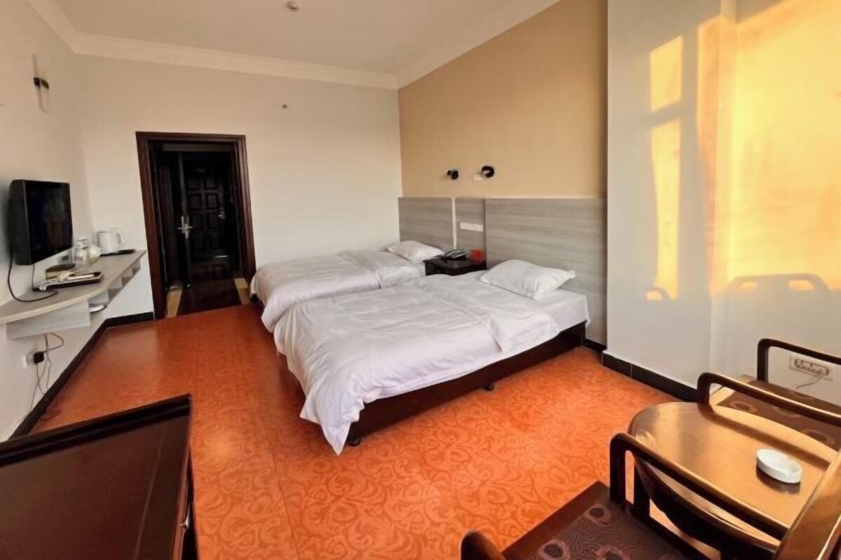 Habitación de hotel con dos camas, un escritorio, un televisor y una ventana con luz solar.