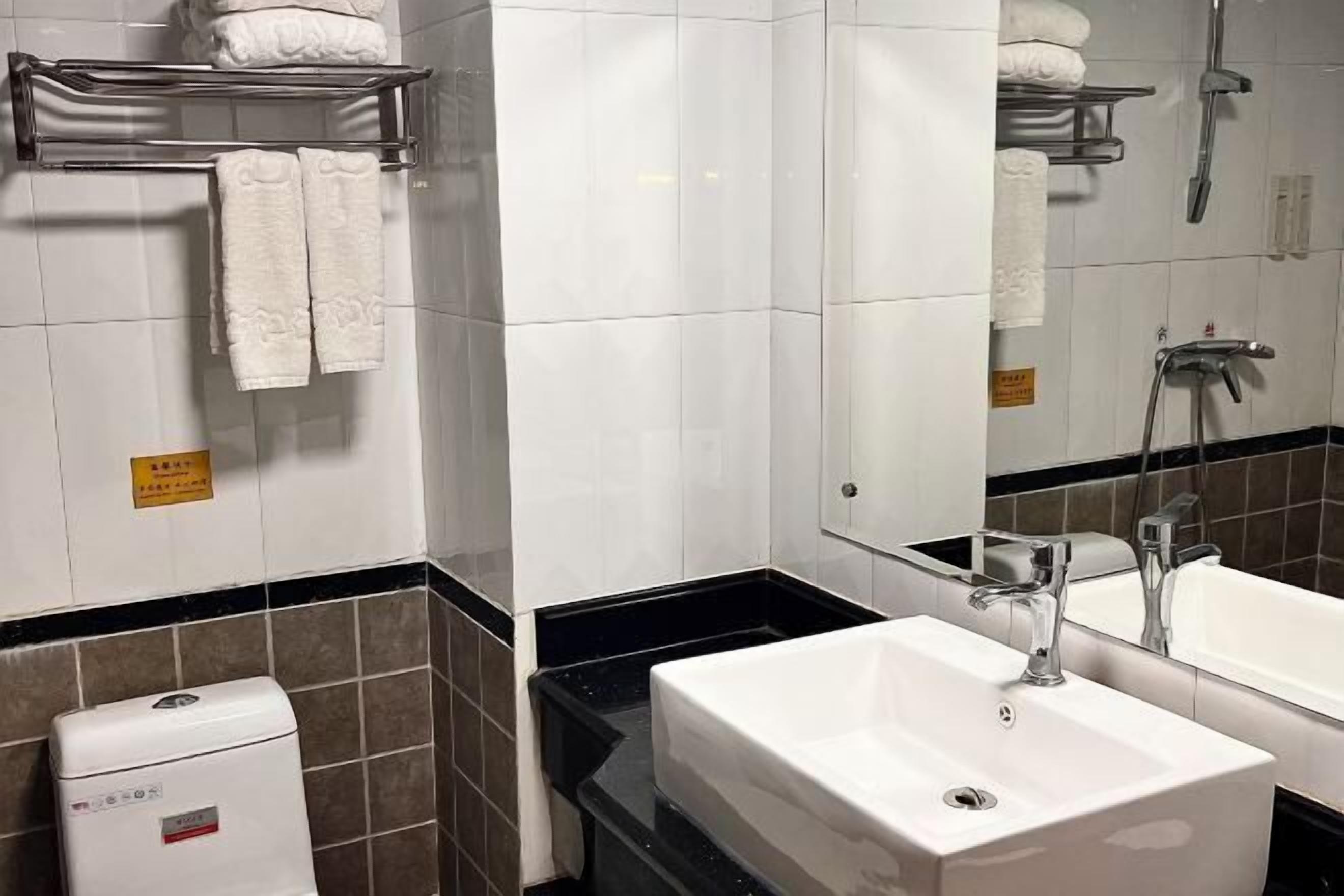A hotel bathroom with a white sink, a mirror, and a towel rack with folded towels.