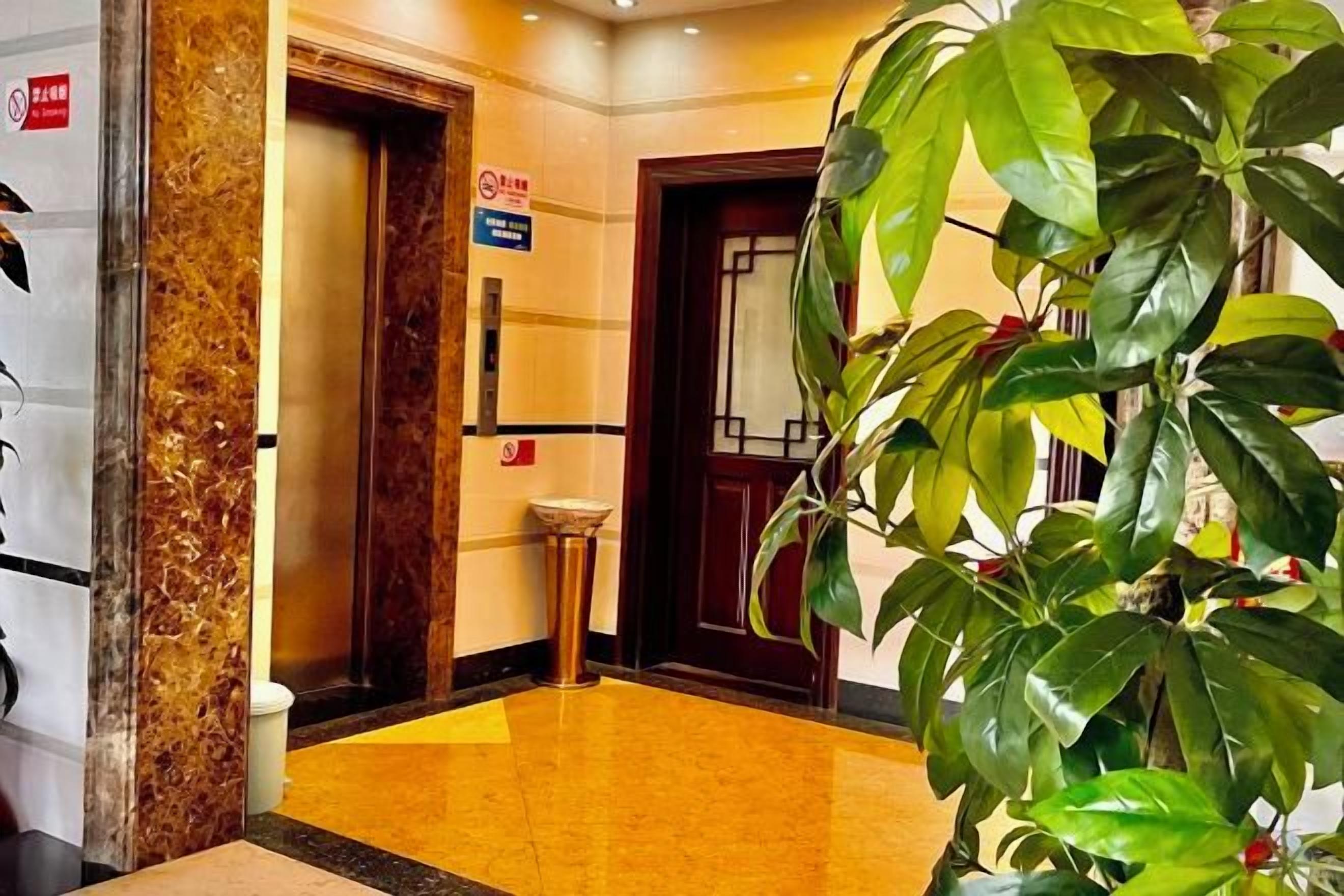 A hotel lobby with a marble floor, a reception desk, and a large potted plant.