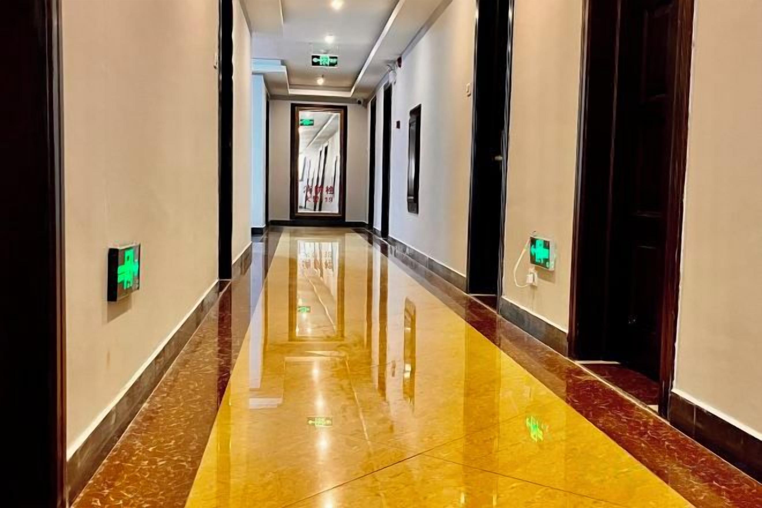 A long, well-lit hallway with a shiny floor, leading to a door at the end.